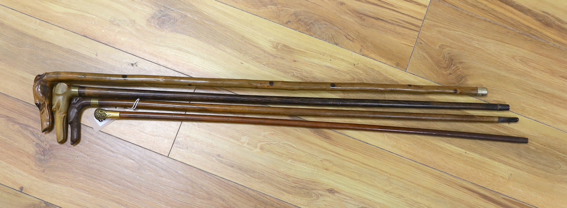Four walking sticks: The first with carved horn dog‘s head handle, two with carved wood dogs head handles, one gilt metal mounted handle, tallest 86cms